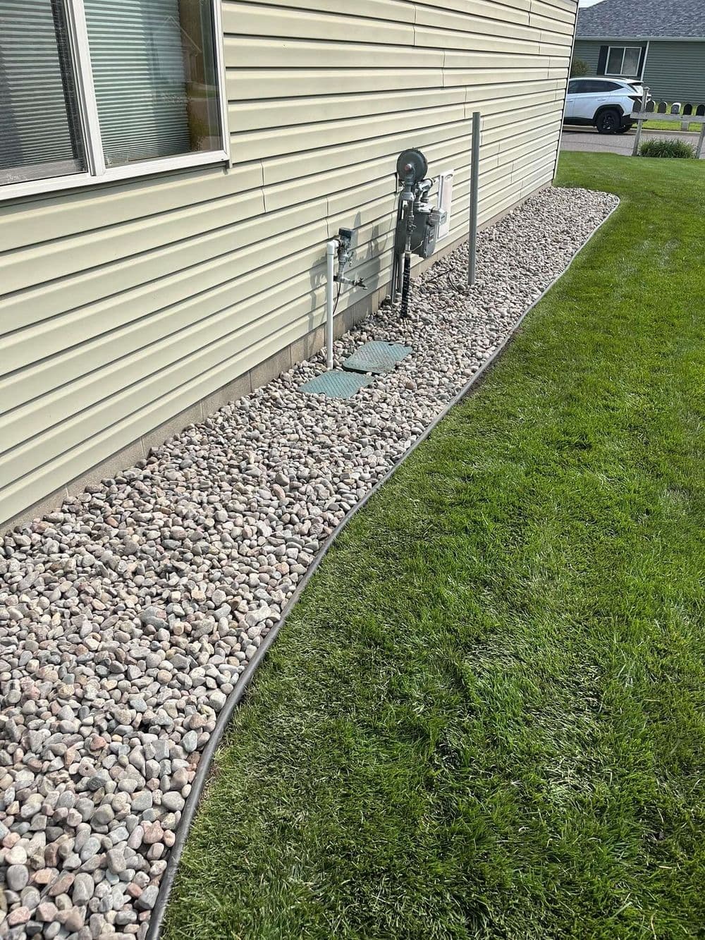 landscaped backyard with pebbled border, utility connections, and green grass lawn